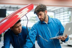 Car mechanic team using laptop boosting car engine at auto repair shop